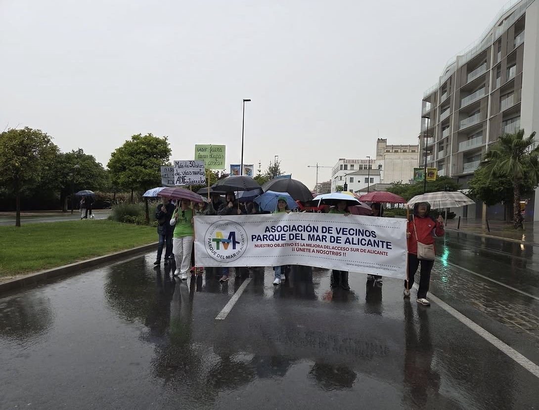 Vecinos con paraguas sostienen la pancarta de la Asociación de Vecinos Parque del Mar de Alicante durante la manifestación