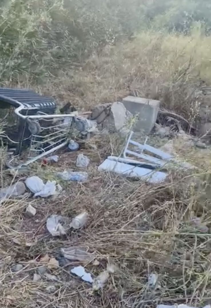 Restos de mobiliario y basura acumulados entre la vegetación en los antiguos terrenos ferroviarios de ADIF